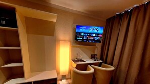 A hotel room with a flat-screen TV mounted on the wall, a small table with a bottle and glasses, and two cushioned chairs.