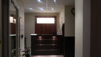 A reception area with a wooden reception desk, a potted plant, and a clock on the wall.