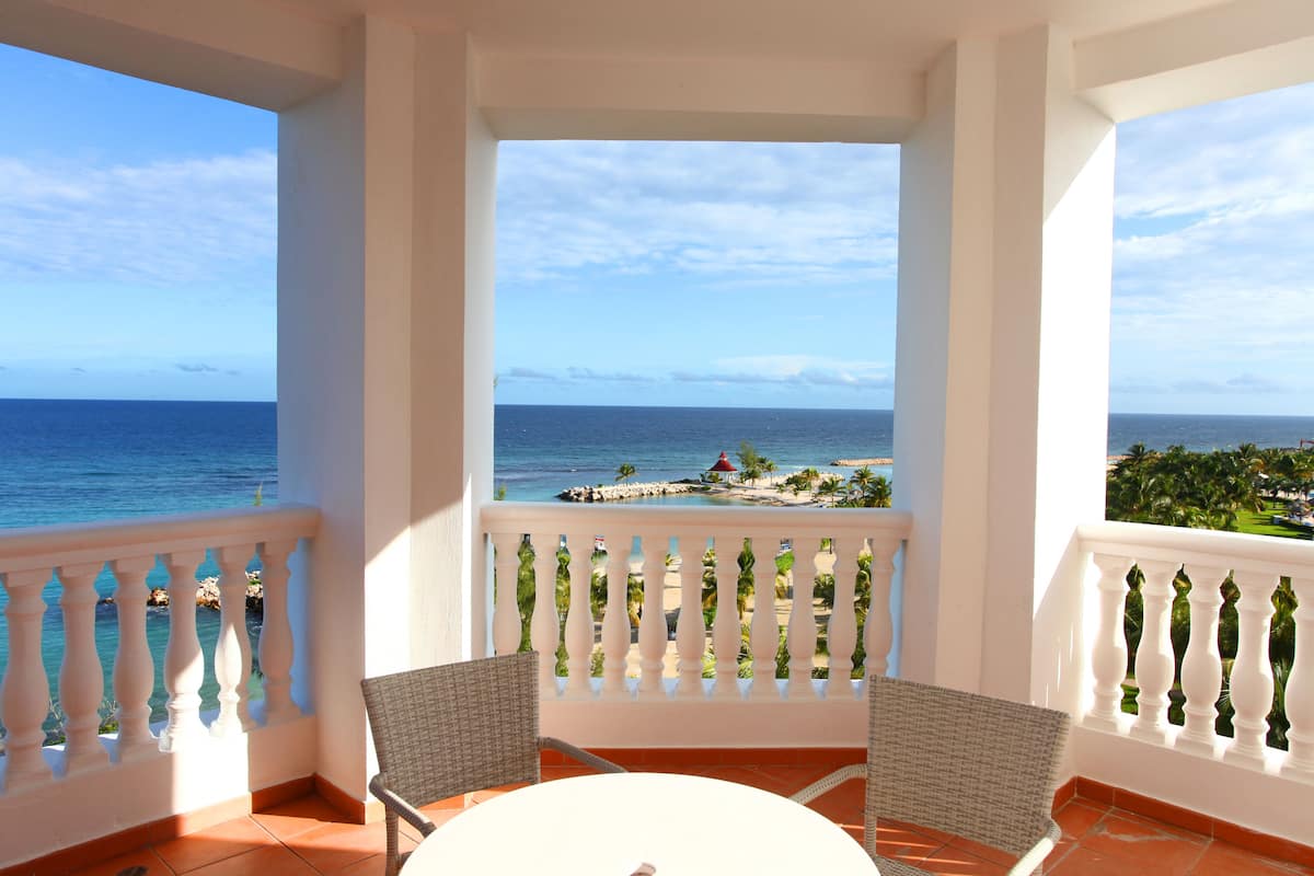 A balcony with a white railing, two wicker chairs, and a small round table.