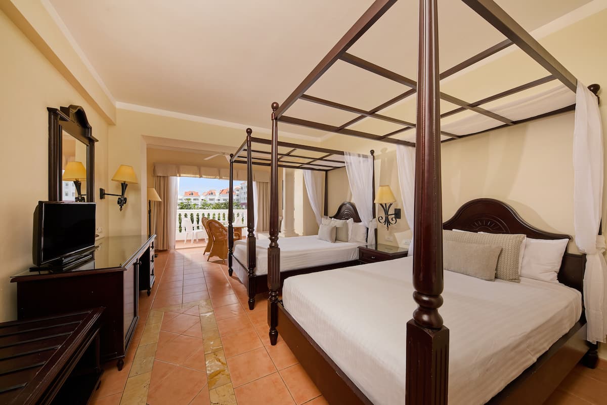 A four-poster bed with a canopy, a television on a wooden stand, and a balcony with a chair.
