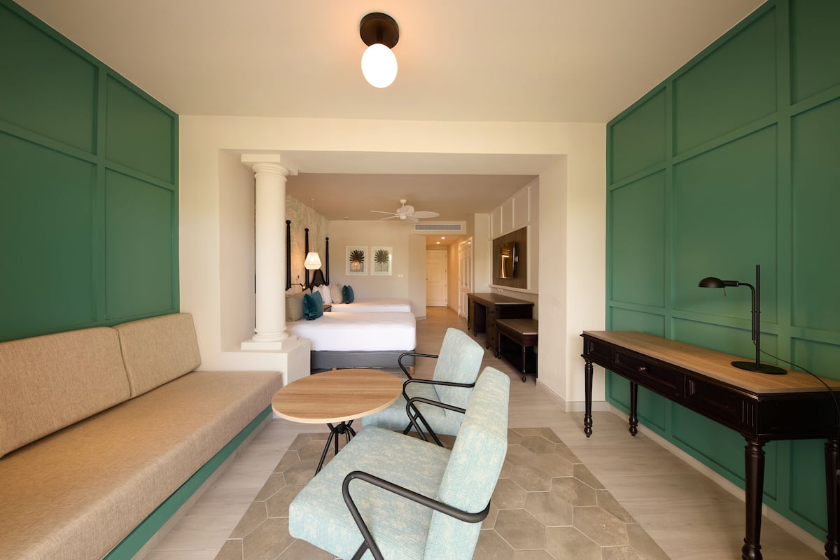 A hotel room with a sofa, two armchairs, a small table, a desk, and a ceiling fan.