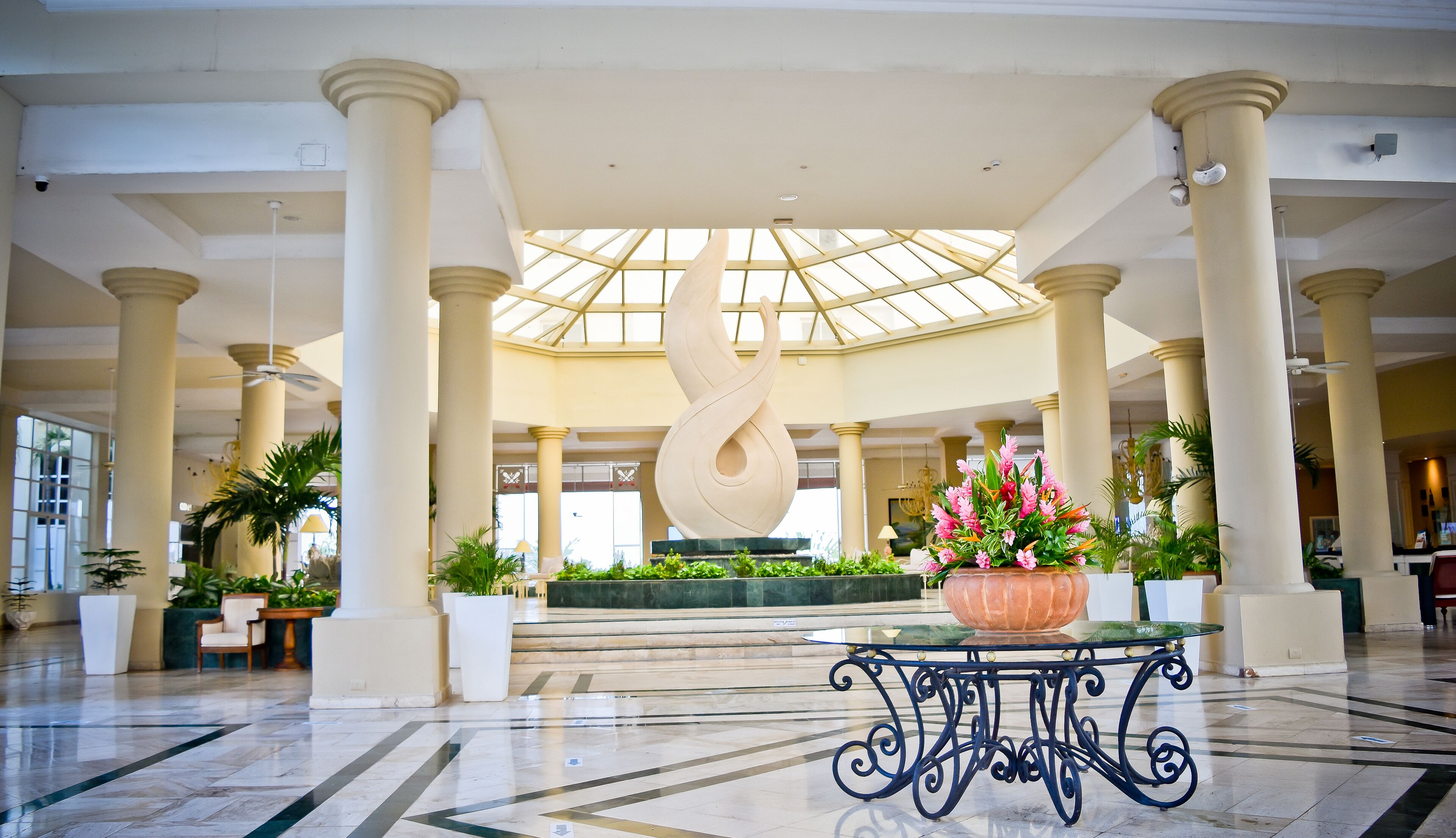 A spacious lobby with a central sculpture, columns, and a glass ceiling.