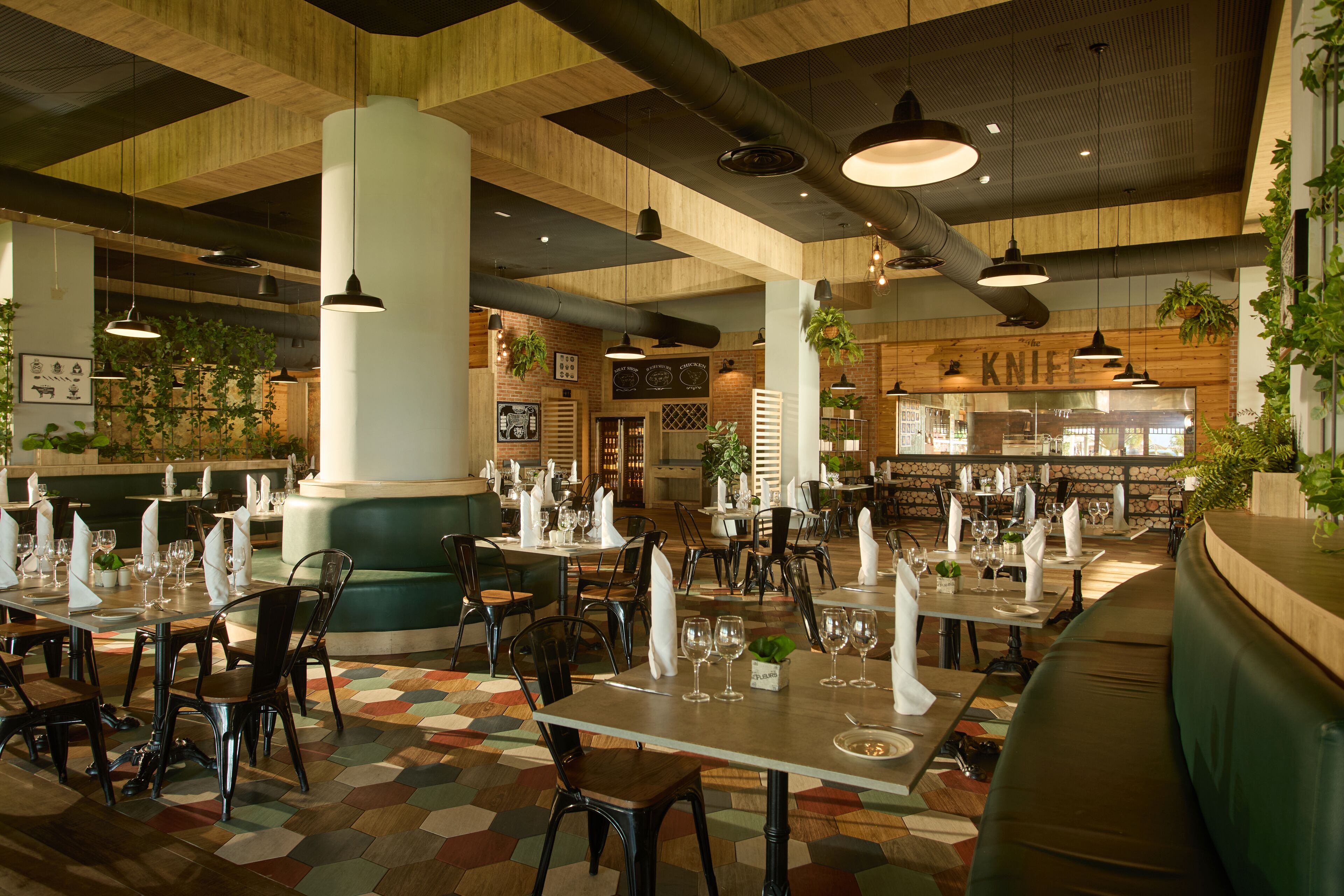 Ein Restaurant mit mehreren Esstischen, gedeckt mit weißen Servietten und Gläsern, umgeben von Stühlen.
