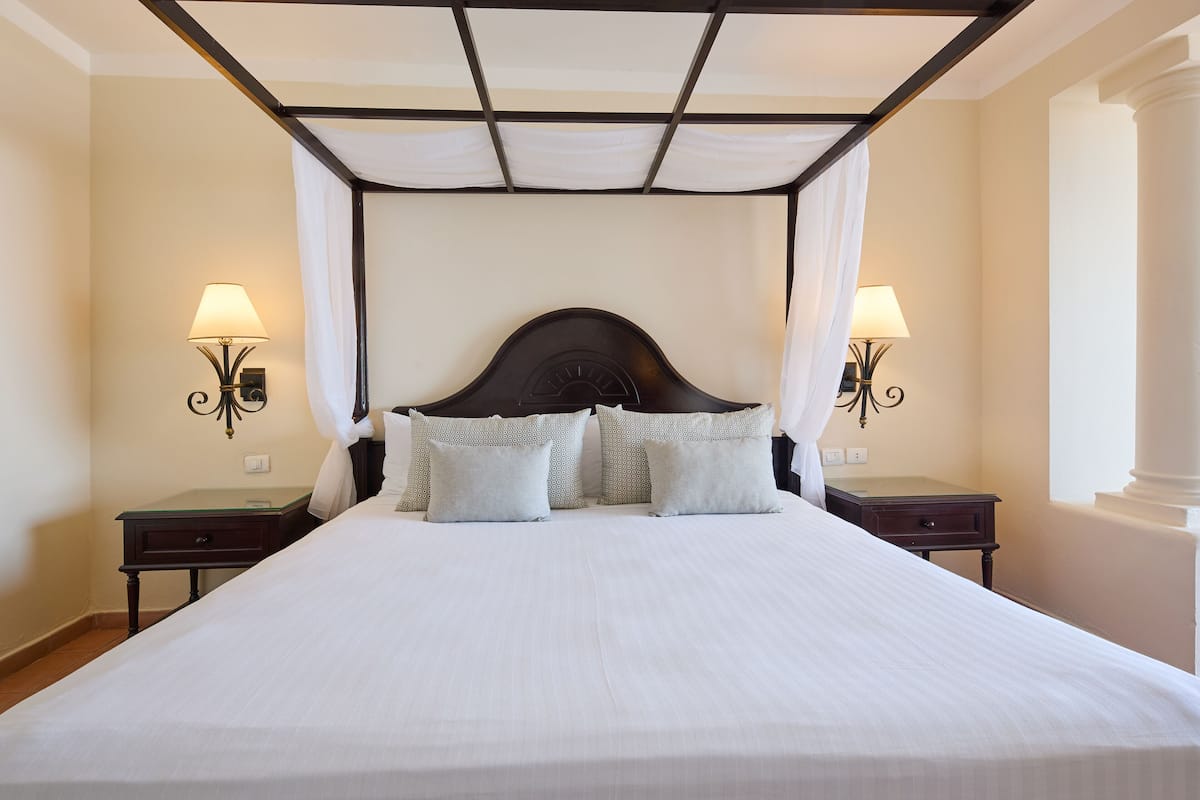 A neatly made bed with a canopy, two bedside tables with lamps, and a large window with a view.