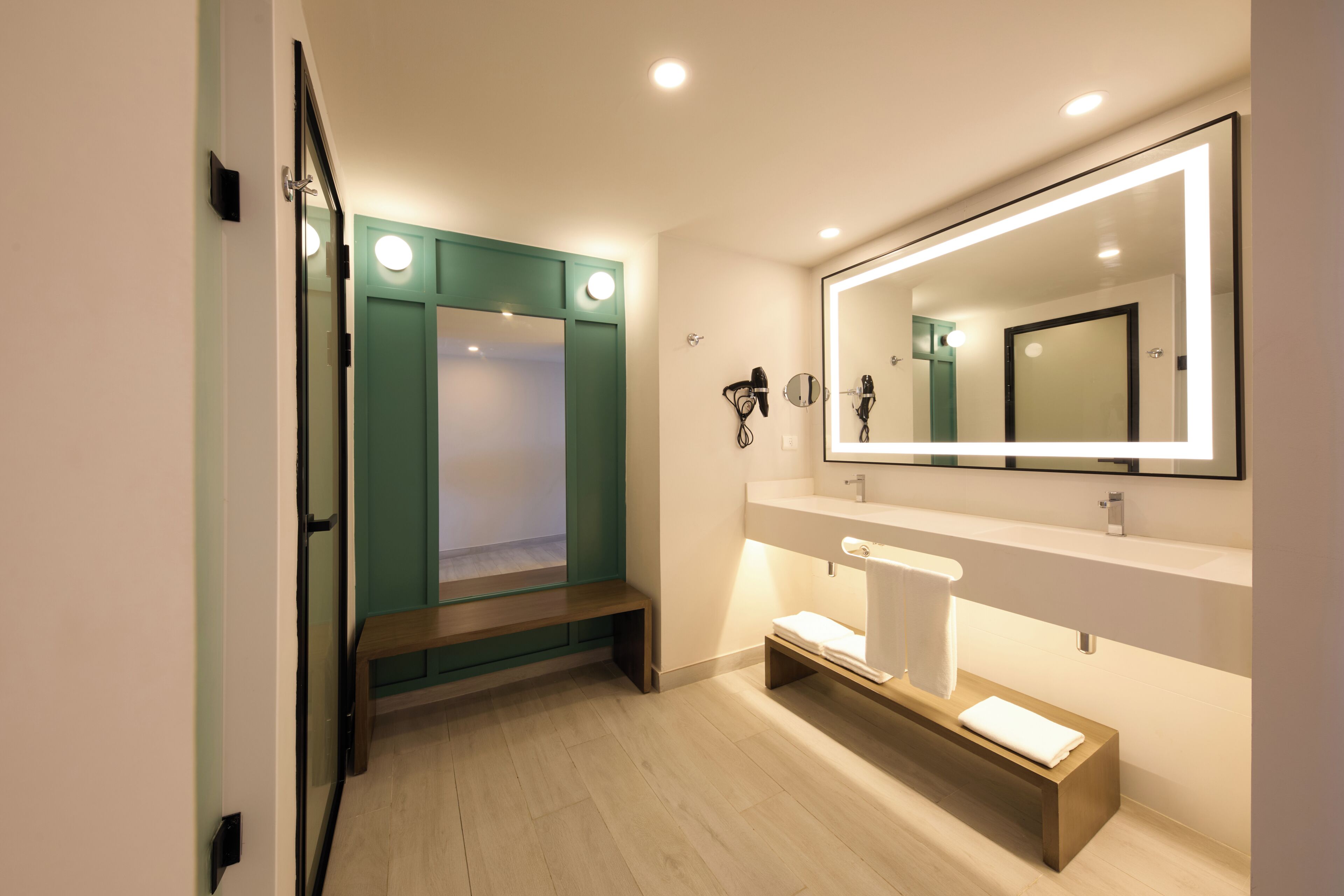 A modern bathroom with a bench, a large mirror, and a vanity with a towel rack.