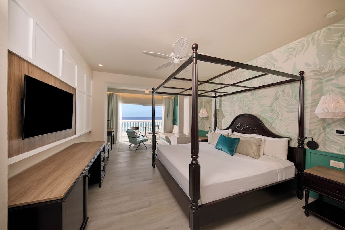 A four-poster bed with a ceiling fan, a flat-screen TV, and a view of the ocean.