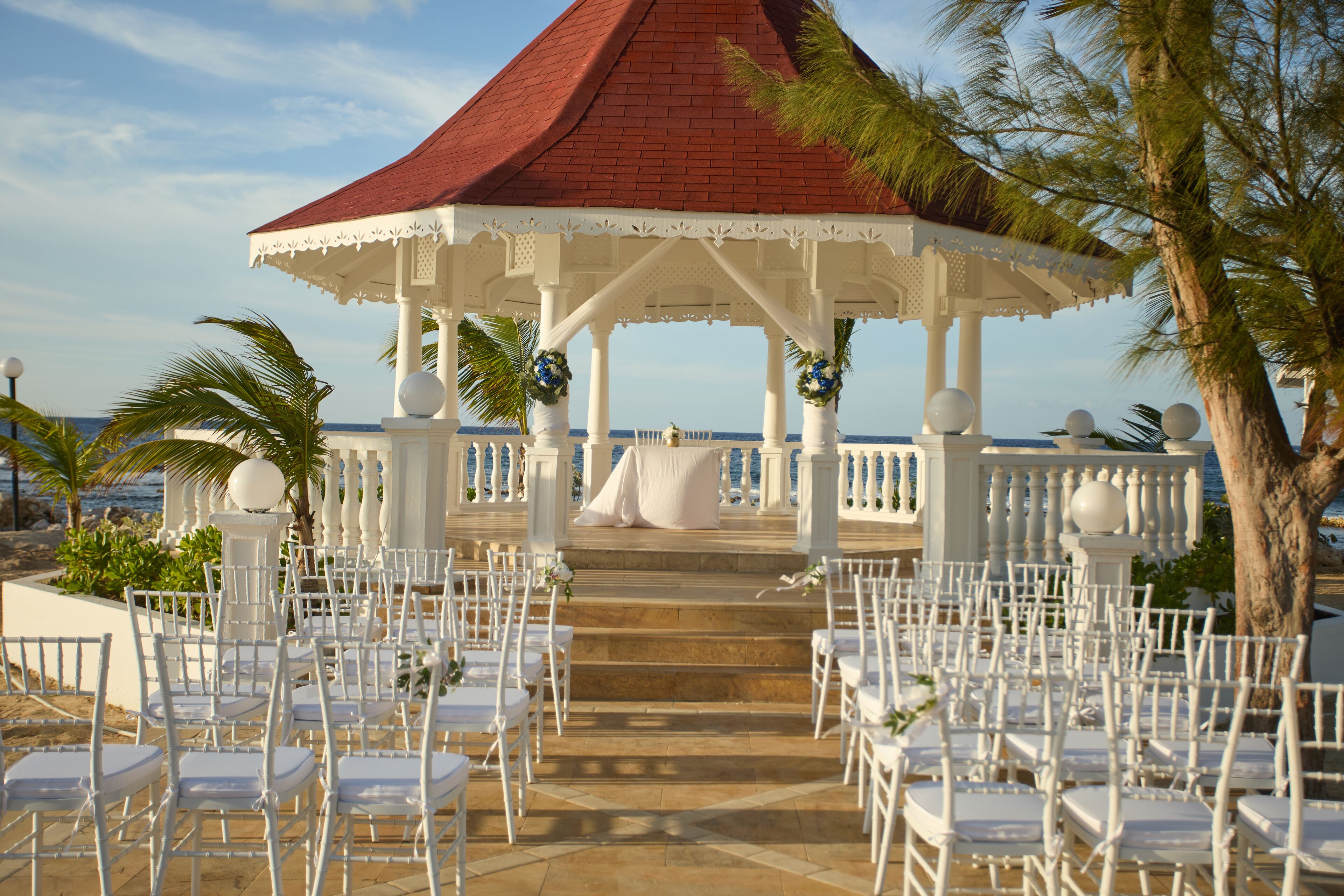 A gazebo with white chairs arranged for an event, overlooking a beach.