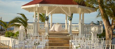 A gazebo with white chairs arranged for an event, overlooking a beach.