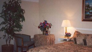 A hotel room with a bed, a chair, a small table with a lamp, a vase of flowers, and a potted plant. - Tahoe Inn (Kings Beach)