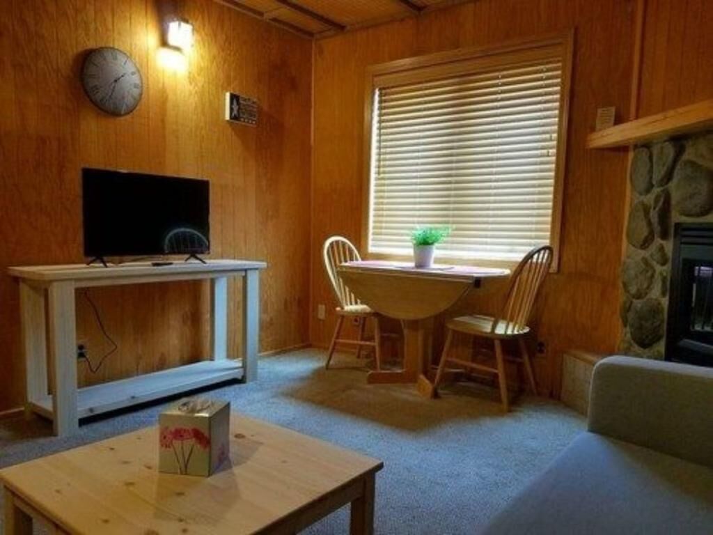 Ein gemütliches Zimmer mit Holzvertäfelung, einem Esstisch mit Stühlen, einem Fernseher auf einem Schrank und einem Kamin.