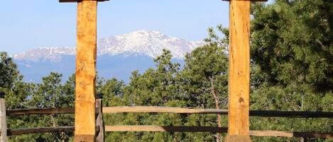 A wooden arch structure with a wooden deck in front, set against a backdrop of trees and mountains.