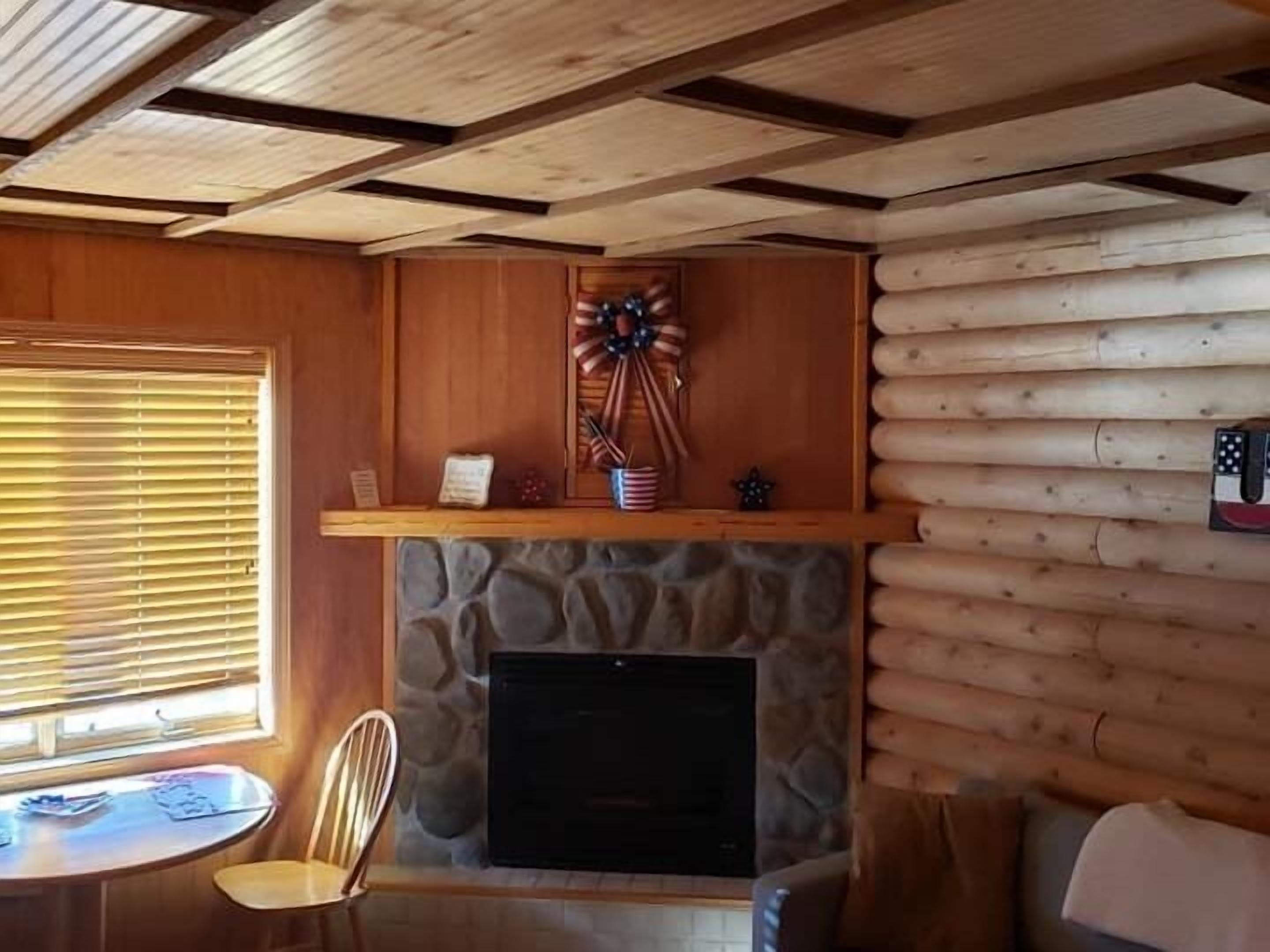 Ein Blockhaus-Interieur mit Kamin aus Stein, Holzwänden und einer Decke mit freiliegenden Balken.