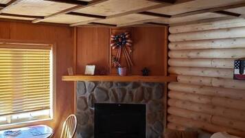 Ein Blockhaus-Interieur mit Kamin aus Stein, Holzwänden und einer Decke mit freiliegenden Balken.