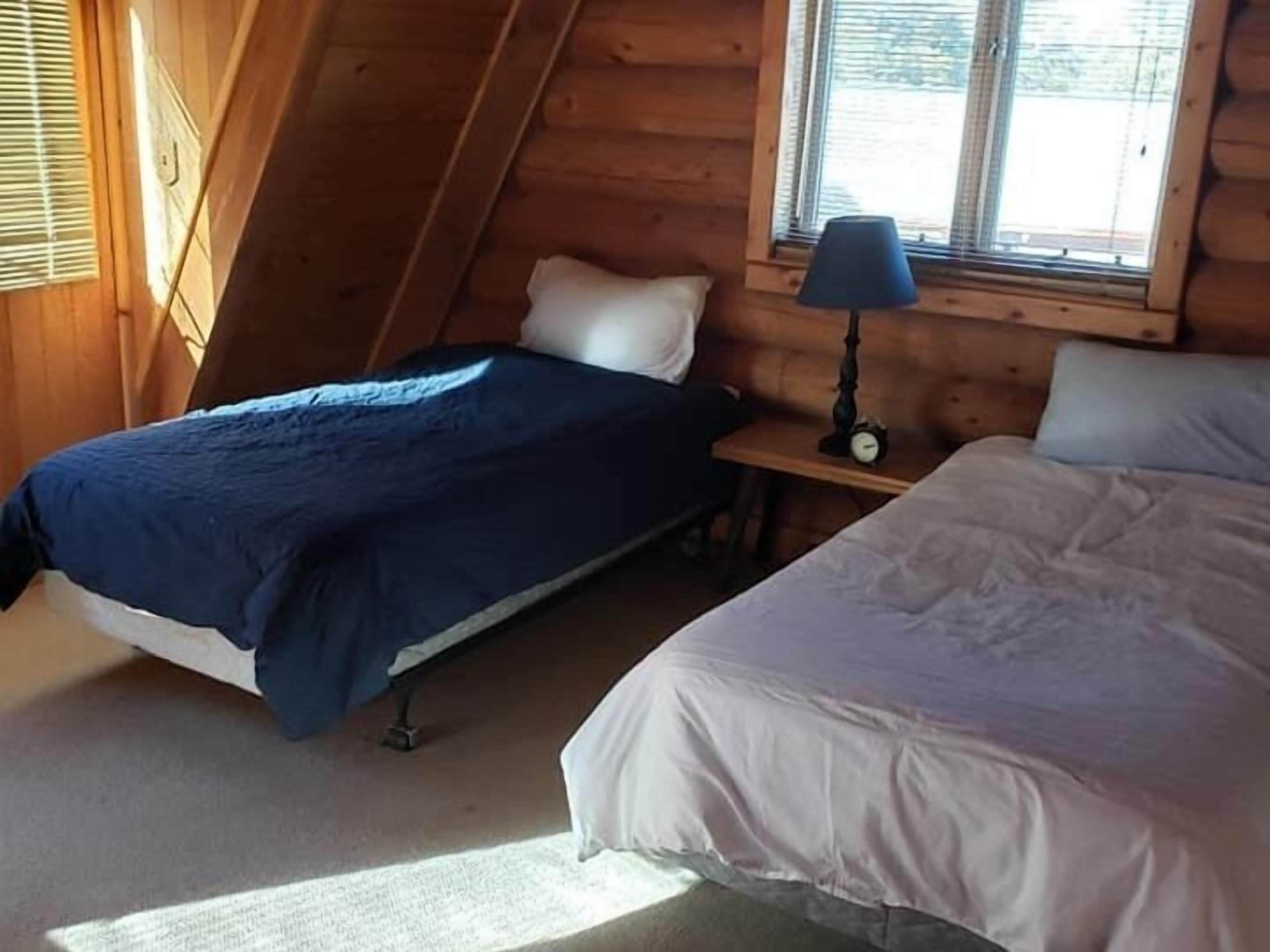 A cabin with two beds, a small table with a lamp, and a window with blinds.