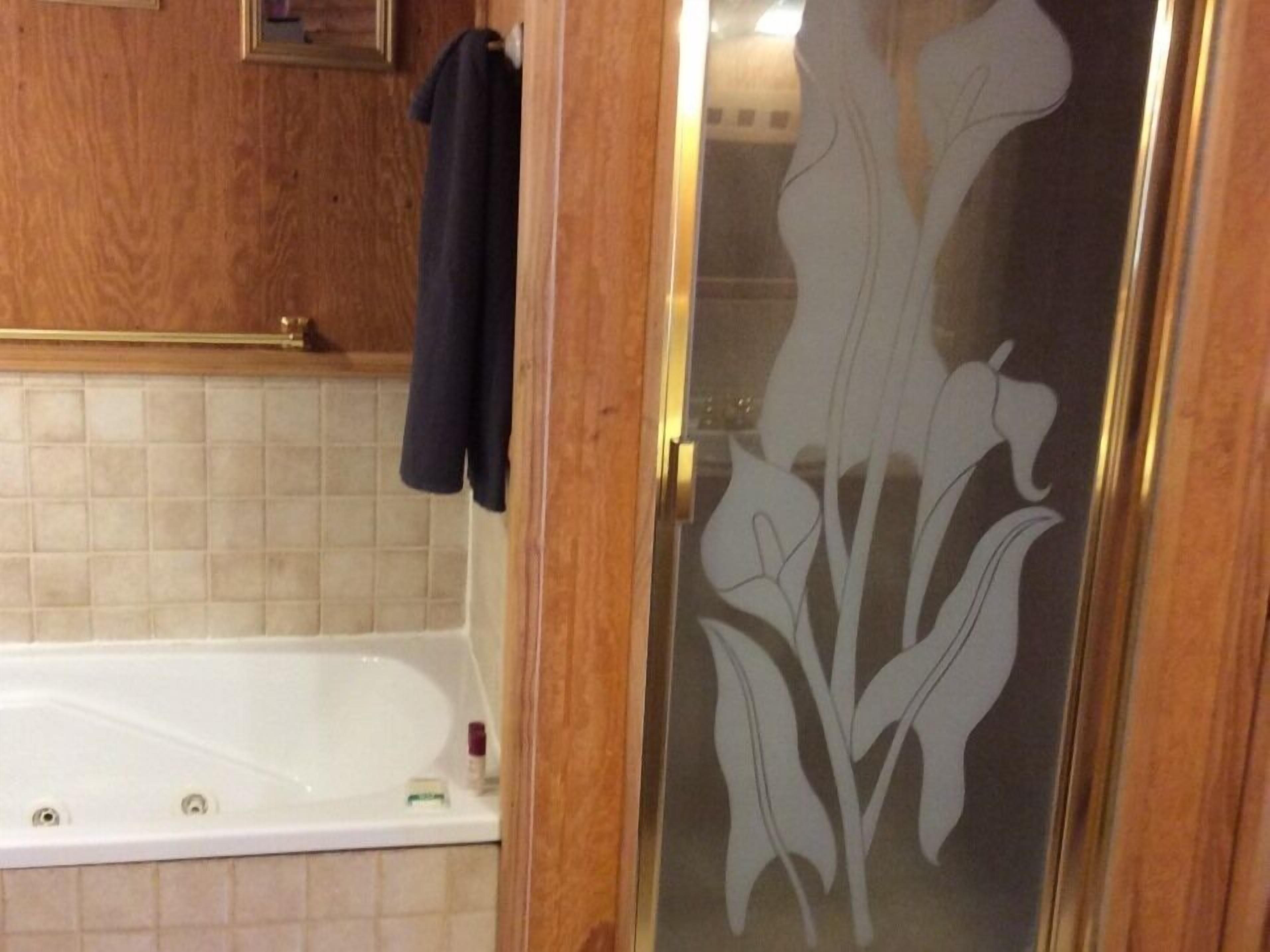 A bathroom with a white bathtub, wooden paneling, and a glass door with a floral design.