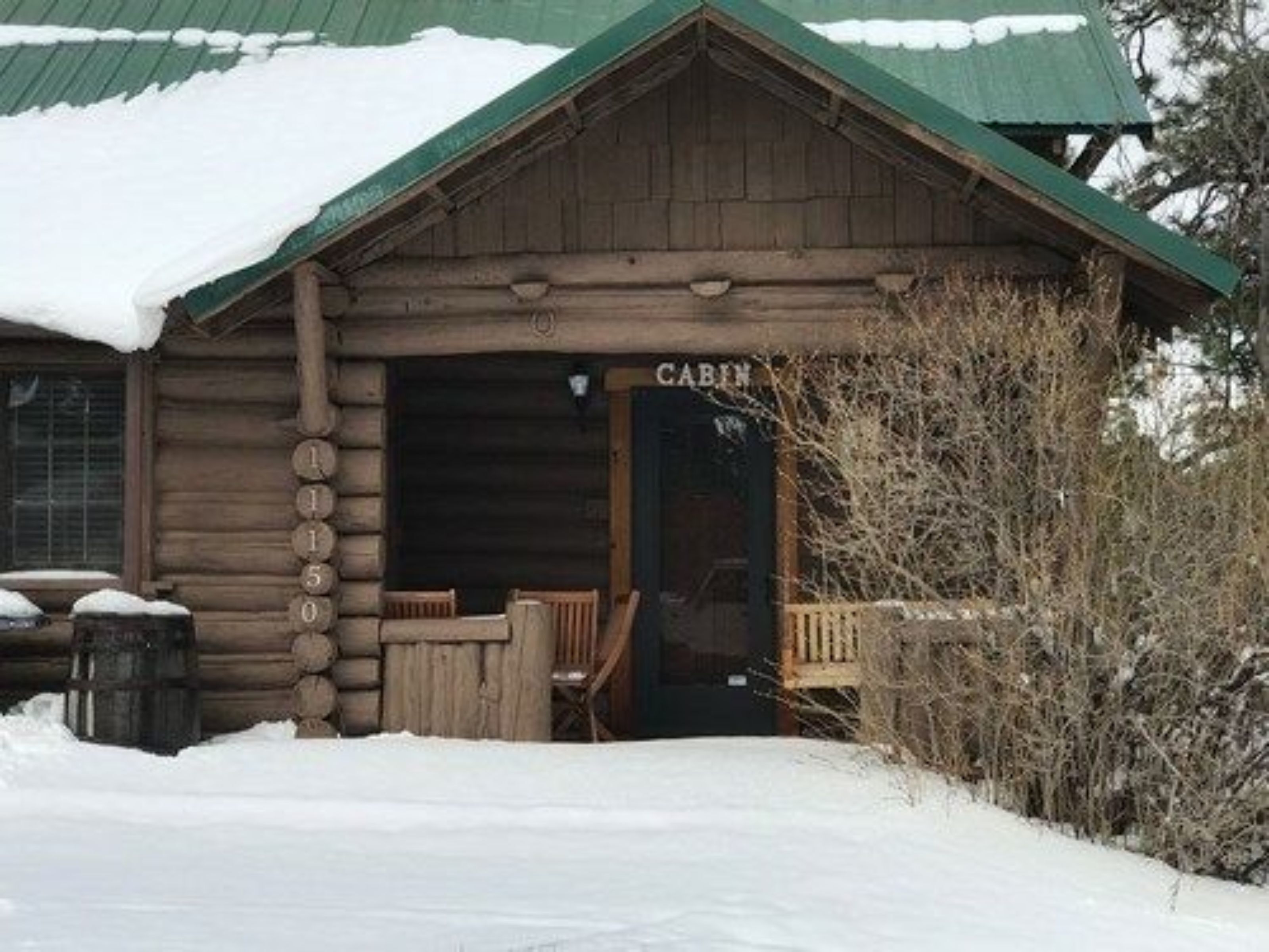 Eine Blockhütte mit einem grünen Dach, einer Holzveranda und einem Schild mit der Aufschrift 'CABIN'.
