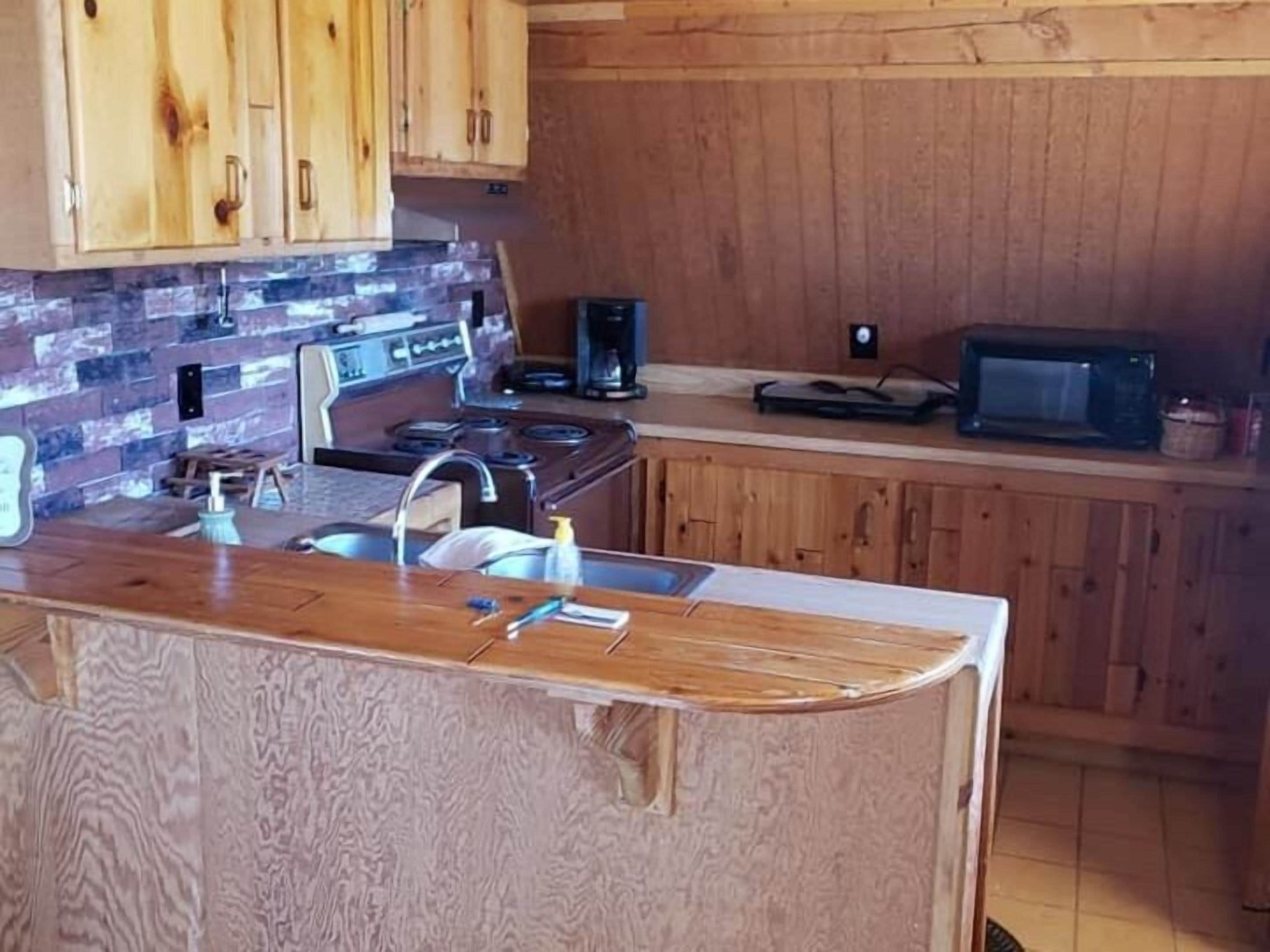 Une cuisine avec des meubles en bois, un plan de travail en granit, une cuisinière, un évier et un four à micro-ondes.