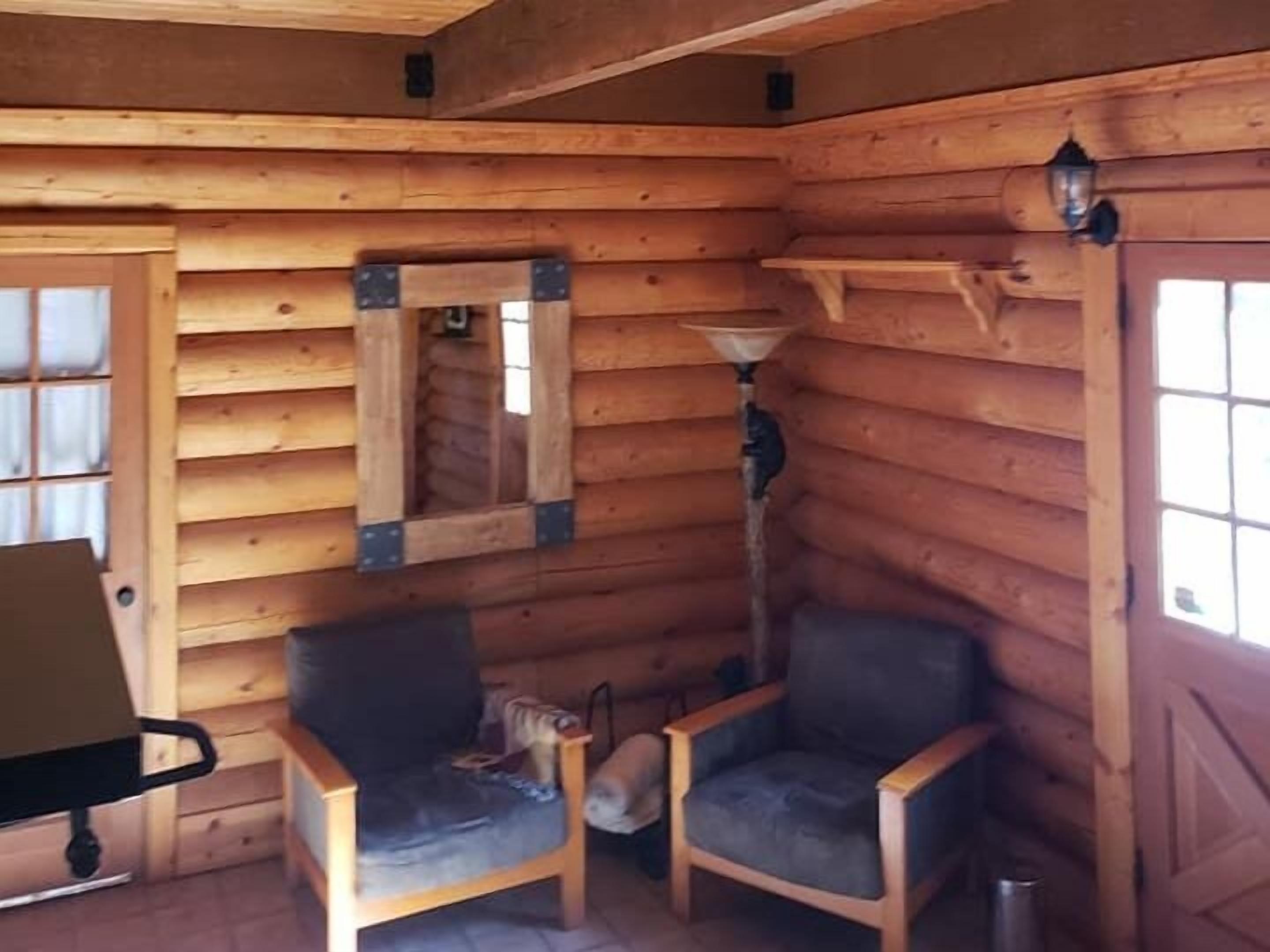 A log cabin interior with two wooden chairs, a small table, and a mirror on the wall.