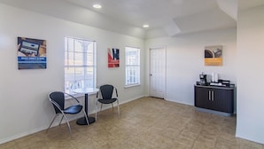 A hotel room with a dining area, two chairs, a table, a coffee station, and artwork on the walls. - Motel 6 Paris, TX (Paris)