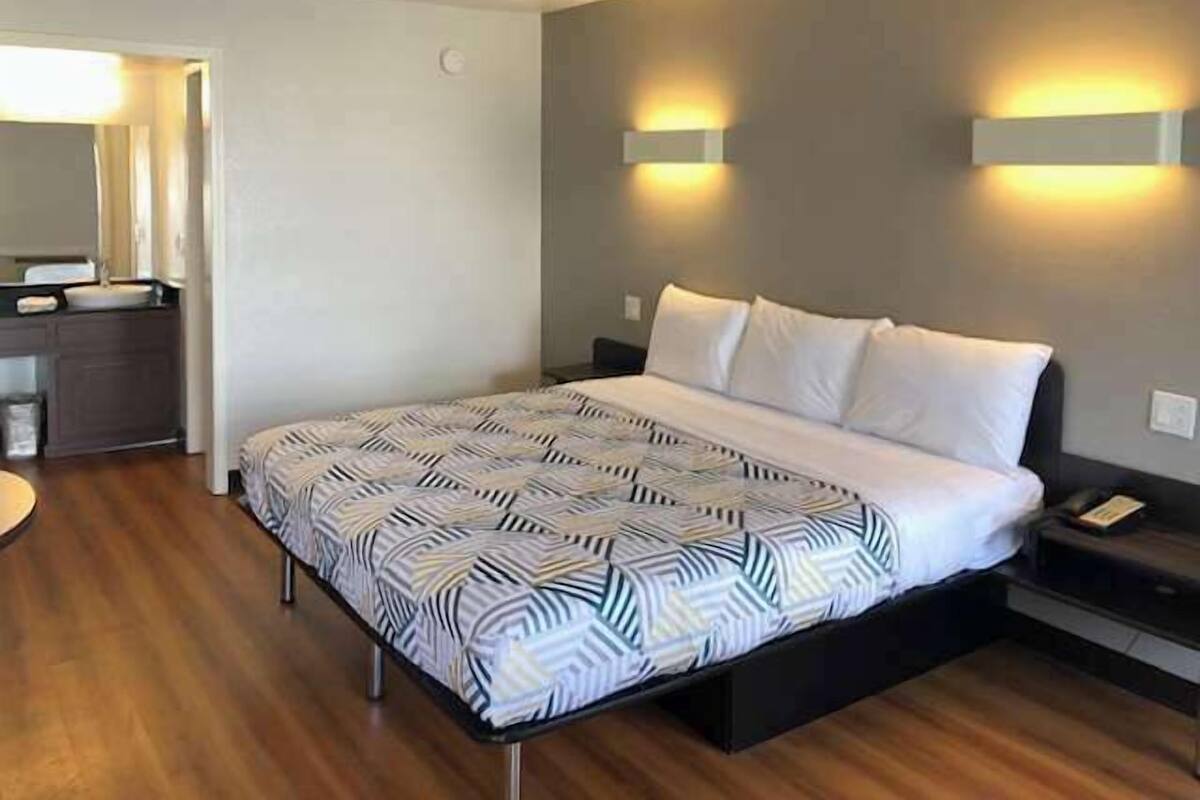 A modern hotel room with a large bed, a bedside table, and a built-in desk with a lamp.