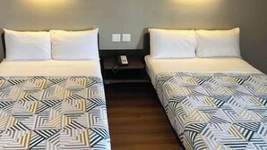 A hotel room with two beds, each with a patterned bedspread and white pillows. There are wall-mounted light fixtures above each bed. - Motel 6 Paris, TX (Paris)