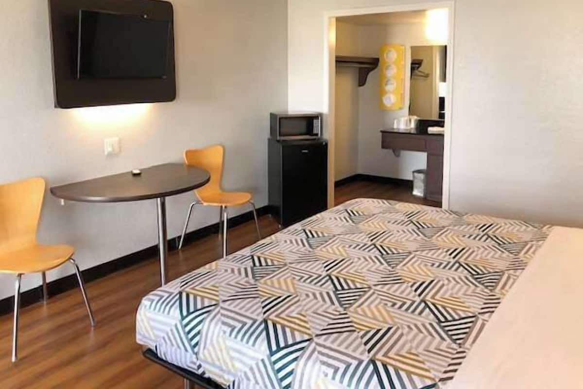 A hotel room with a bed, a desk with two chairs, a television, and a small kitchenette.