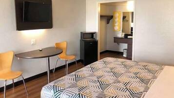 Una habitación de hotel con una cama, un escritorio con dos sillas, un televisor y una pequeña kitchenette.