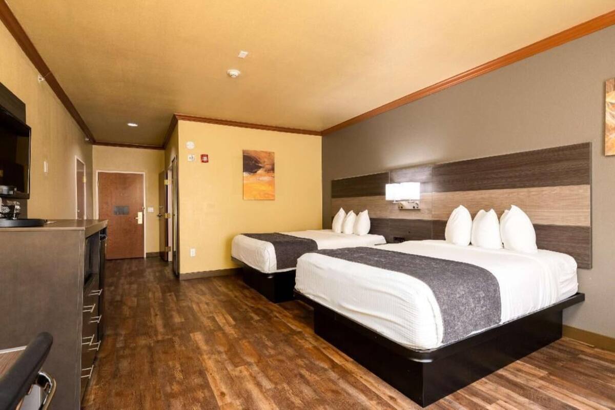 A hotel room with two beds, a kitchenette, a wooden floor, and a painting on the wall.