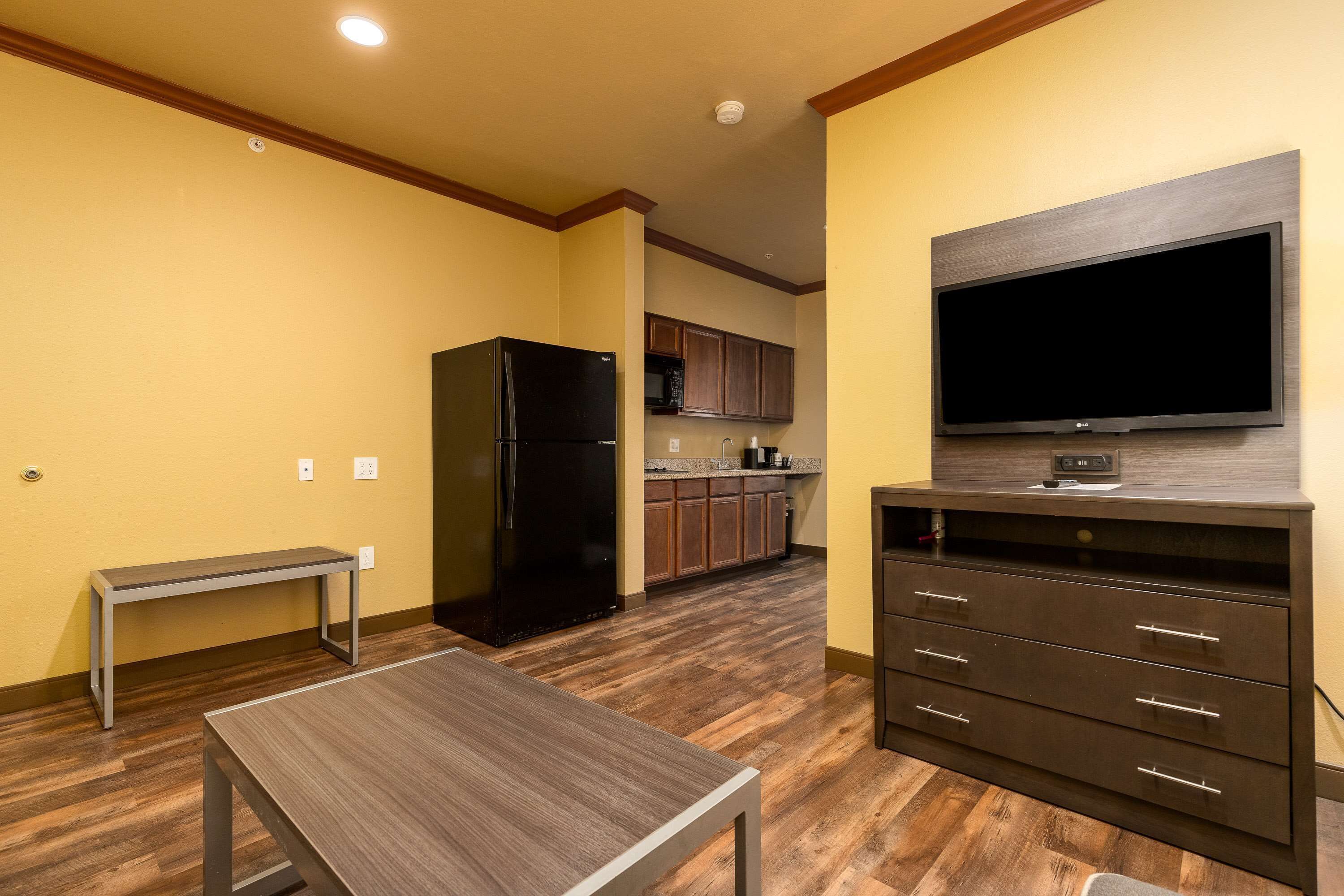 A modern kitchen with a built-in microwave, a black refrigerator, and a flat-screen TV mounted on a wooden cabinet.