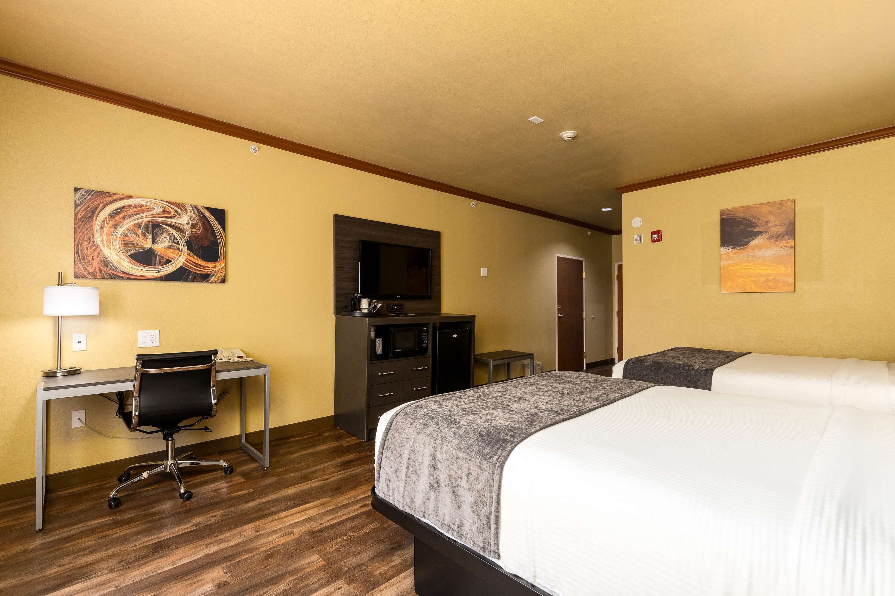 A hotel room with a bed, desk, chair, and artwork on the walls.