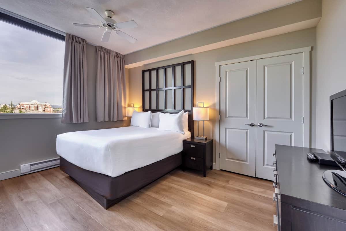 Habitación de hotel moderna con una cama grande, ventilador de techo, vista a la ciudad y un escritorio con computadora.