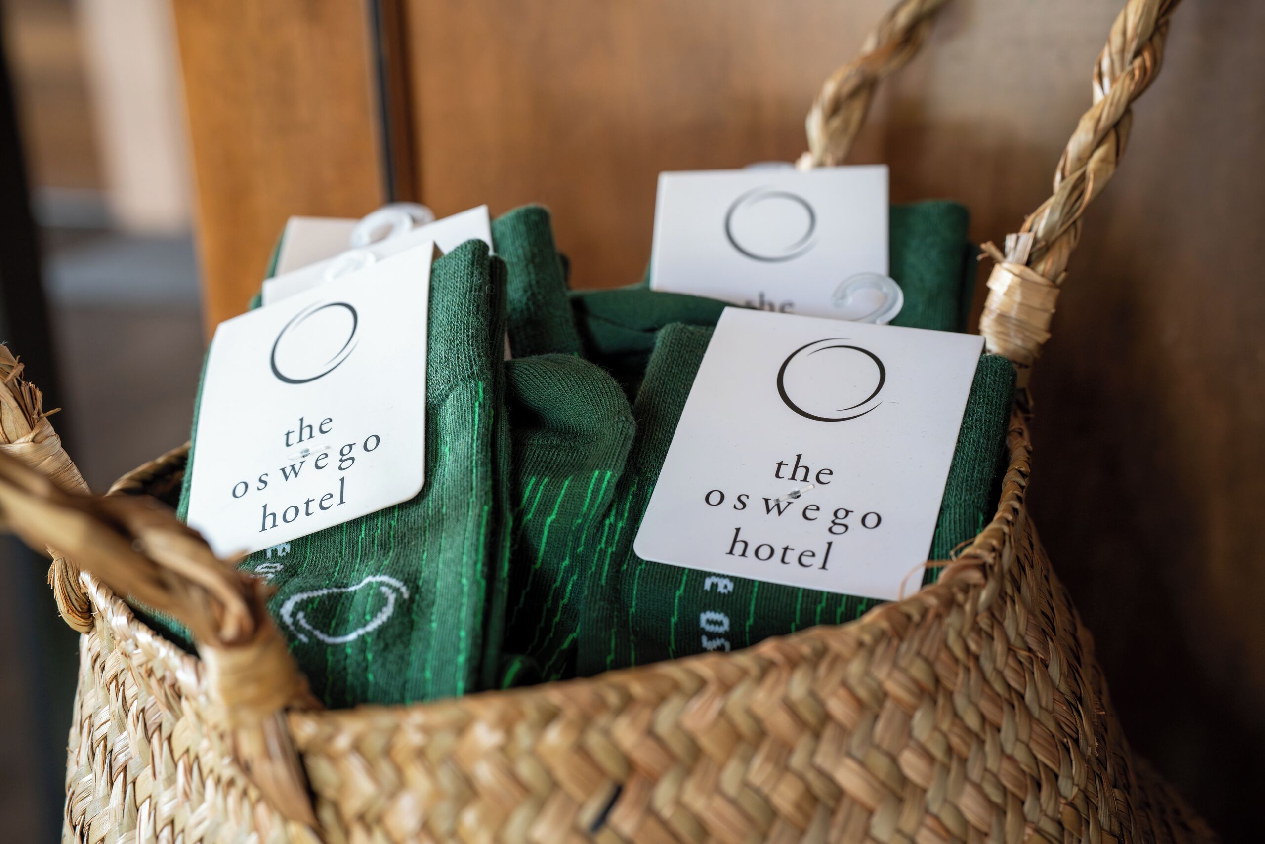 A basket containing green towels with tags that read 'the oswego hotel'.