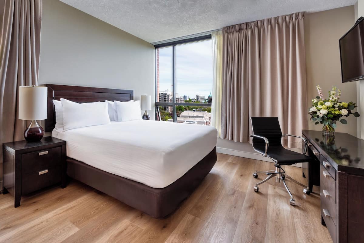 Habitación de hotel con una cama grande, un escritorio, una silla, un televisor y vistas a la ciudad.