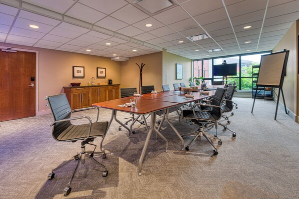 A conference room with a large table, chairs, a TV, and a whiteboard.