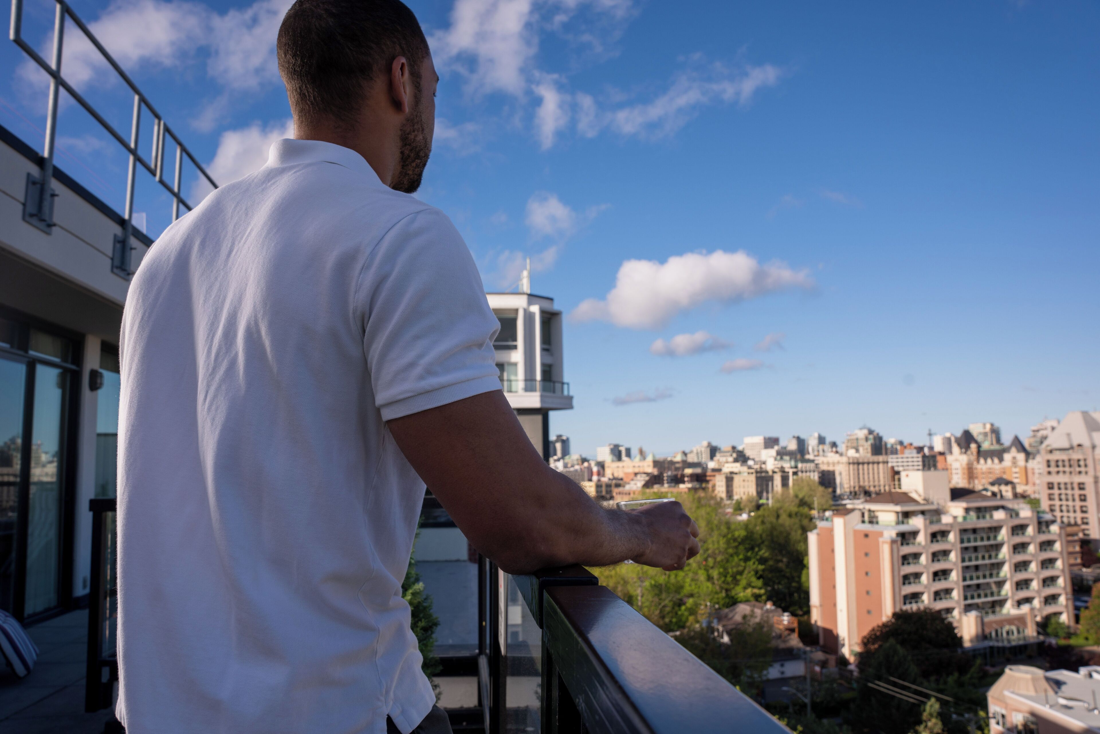 Una persona de pie en un balcón con vistas a un paisaje urbano de edificios y árboles.