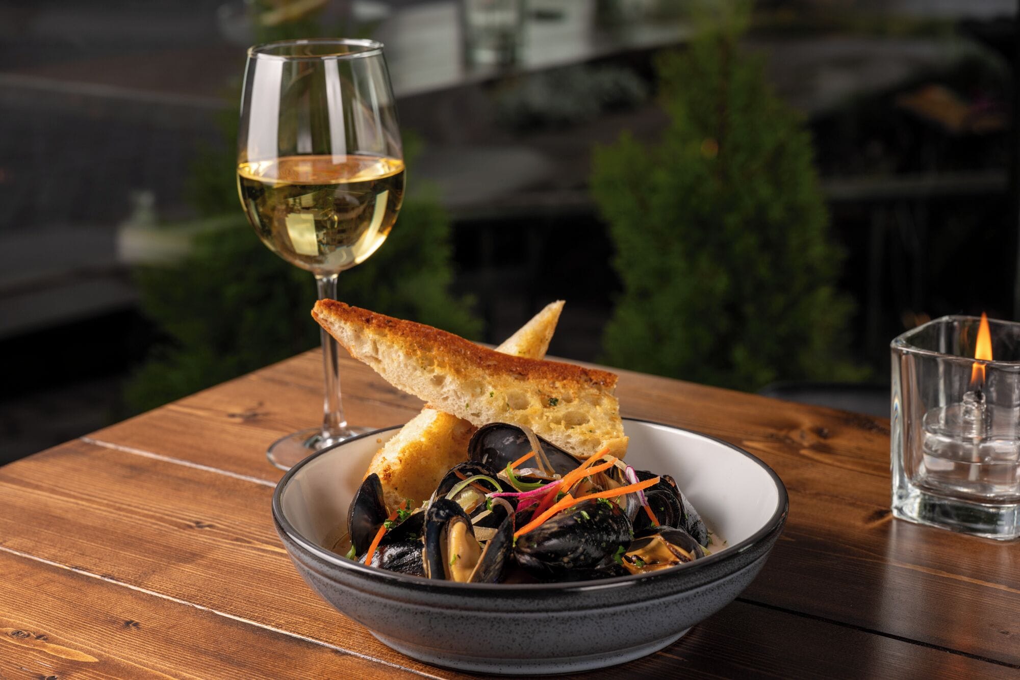 Eine Schüssel mit Muscheln, Brot und einem Glas Weißwein auf einem Holztisch.