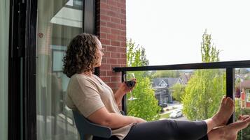 Une personne assise sur une chaise de balcon, tenant un verre de vin, avec en arrière-plan une vue sur des maisons et des arbres.