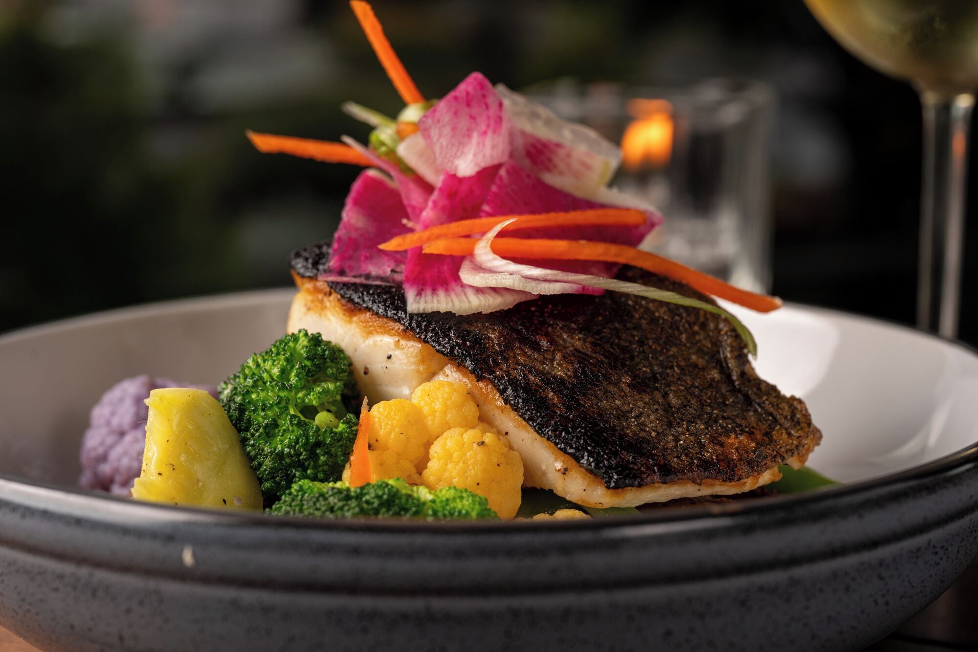 A plate of food with a fish fillet, broccoli, cauliflower, and purple potato.