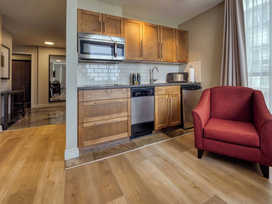 A modern kitchen with wooden cabinets, stainless steel appliances, and a red armchair.