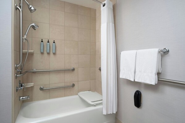 A modern bathroom with a bathtub, grab bars, a showerhead, and a towel rack.