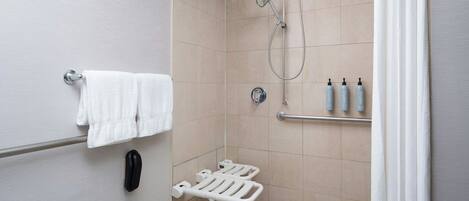 A bathroom with a shower, grab bars, a towel rack, and toiletries.