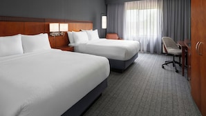A hotel room with two beds, a desk, a chair, a wardrobe, and a large window with curtains.