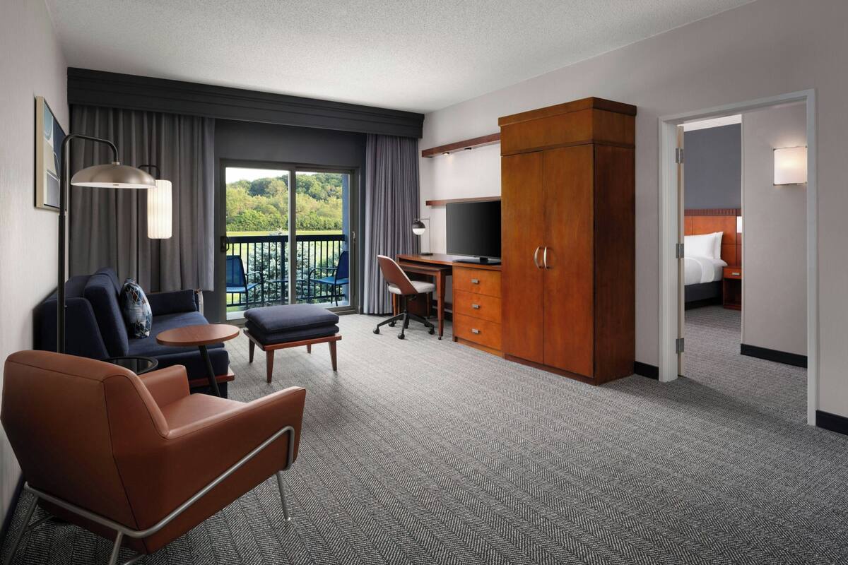 Ein Hotelzimmer mit einer Couch, einem Sessel, einem Schreibtisch, einem Fernseher und einem Kleiderschrank.