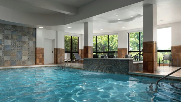 An indoor swimming pool with clear water, stone-tiled walls, and large windows offering views of greenery.
