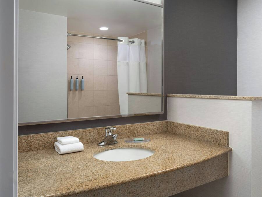Een badkamer met een wastafel met een granieten blad, een spiegel en een douche die op de achtergrond zichtbaar is.