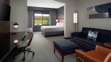 A hotel room with a bed, a desk, a chair, a sofa, and a TV.