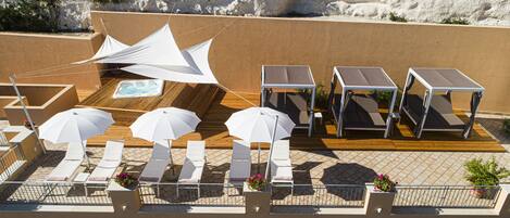 A rooftop terrace with sun loungers, umbrellas, and a pool table.