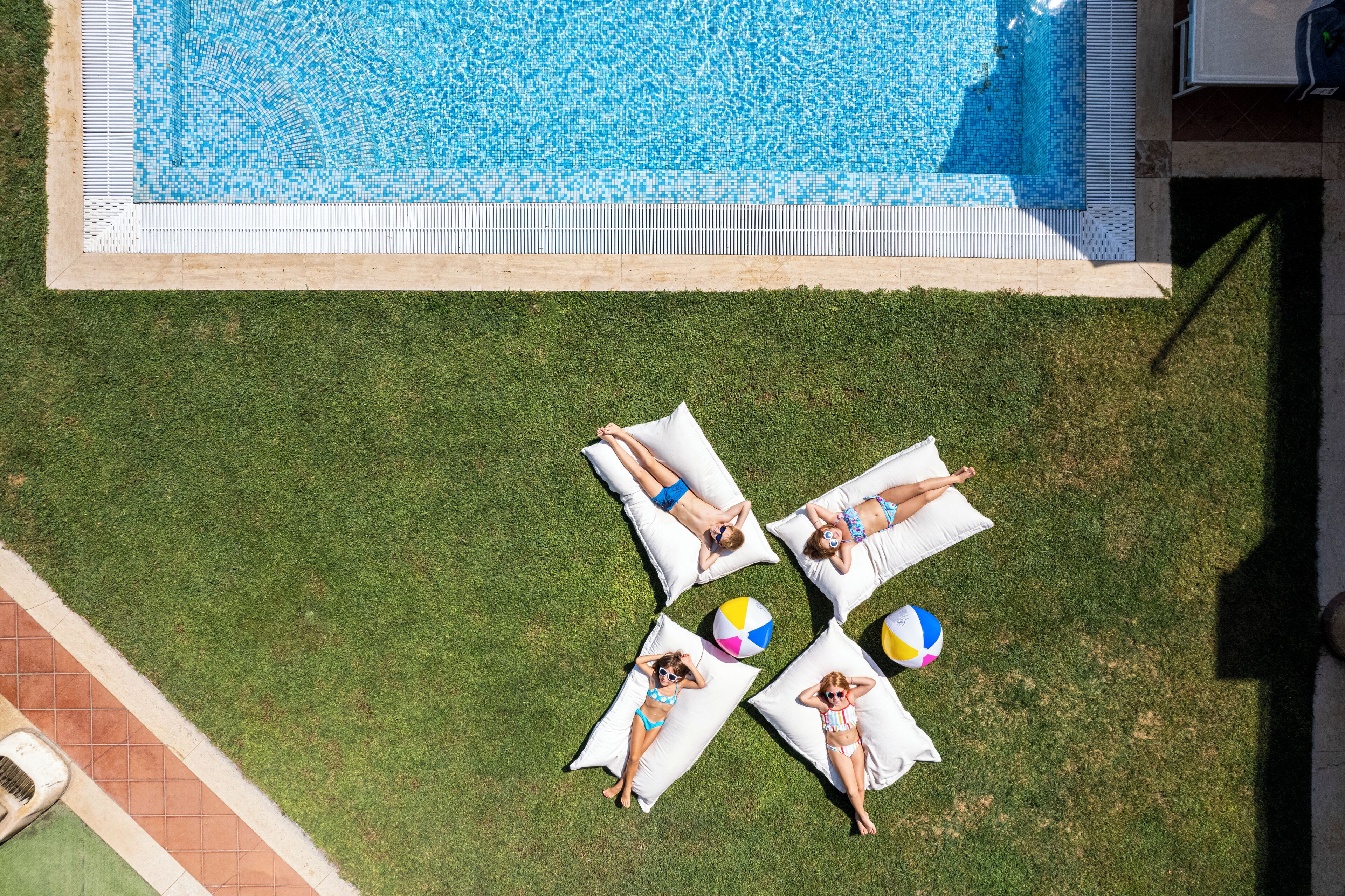 An aerial view of a swimming pool area with four sun loungers and two beach balls.