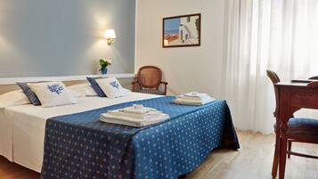 A hotel room with a bed, a chair, a table, a lamp, and a painting on the wall.