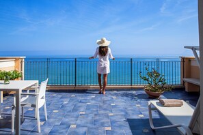 A woman in a white dress and hat standing on a balcony with a view of the sea.